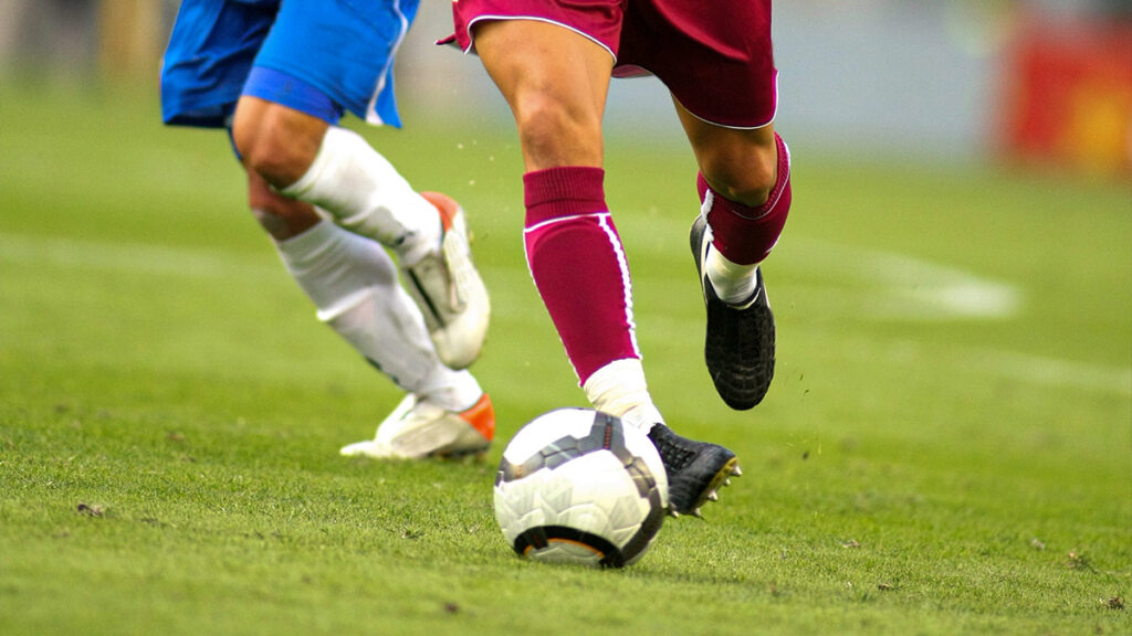 legs of two football players with the ball