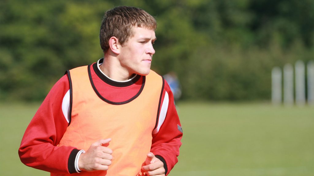 A rugby player, wearing a bib, runs and warms-up.