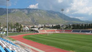 Grass pitch with running track around it and mountain in the background at Sportcamp Loutraki, Greece