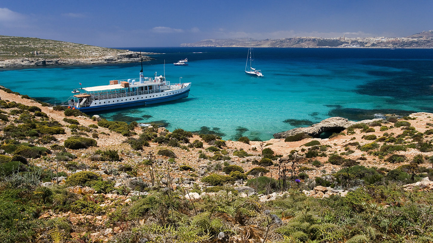 Boat travelling on crystal blue waters as it explores the island of Comino, Malta.