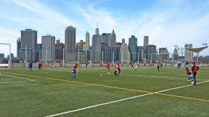 Football game on a rooftop pitch with New York skyline in the background.