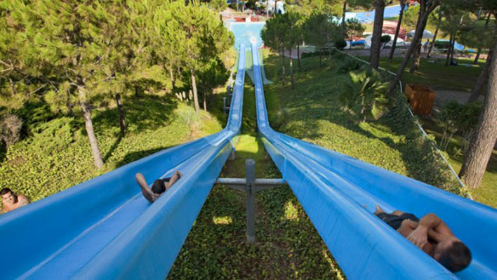 Two children zoom down two water flumes in a theme park.
