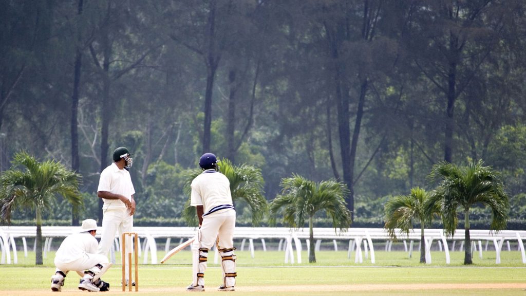 Batsman wait to be bowled at with a forest in the background.