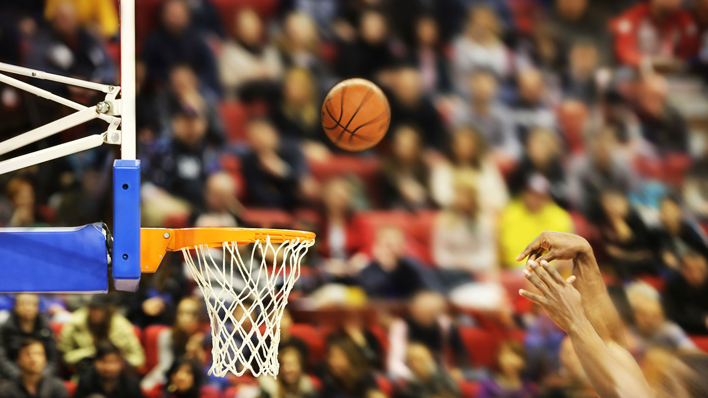 Hands throw the basketball to the hoop, with spectators watching on.