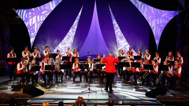 Orchestra on stage with a purple background performing at Disneyland® Paris with a conductor.