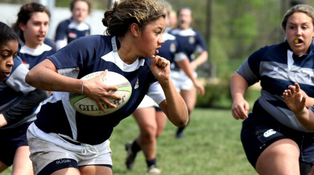 Girl rugby players chase the player holding the ball