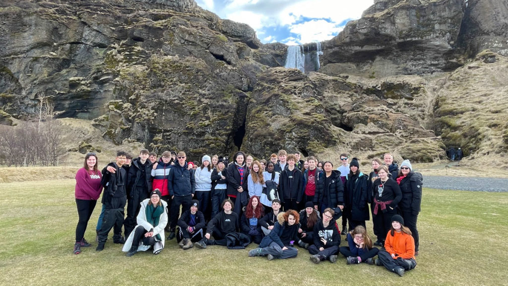 School group pose for a photo in front of a waterfall in Iceland