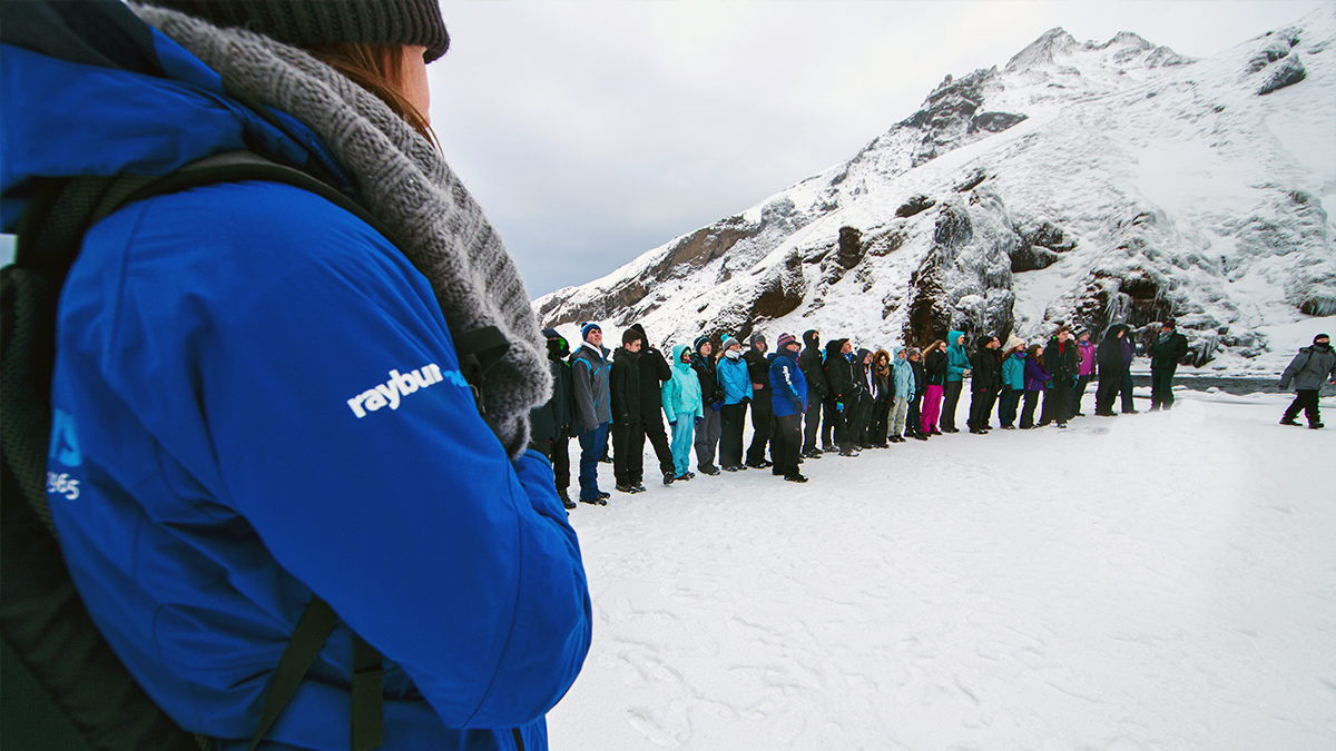 Two Field Study Tutors, one near the camera and the other midground centre, stand in front of a curved line of students on a glacier.
