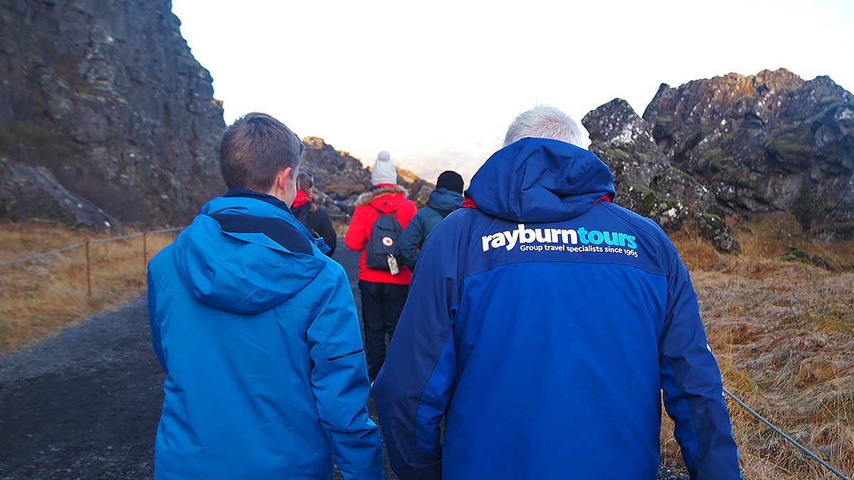 Field Study Tutor, with a Rayburn Tours coat, walks at the back of a group of students whilst talking to a student