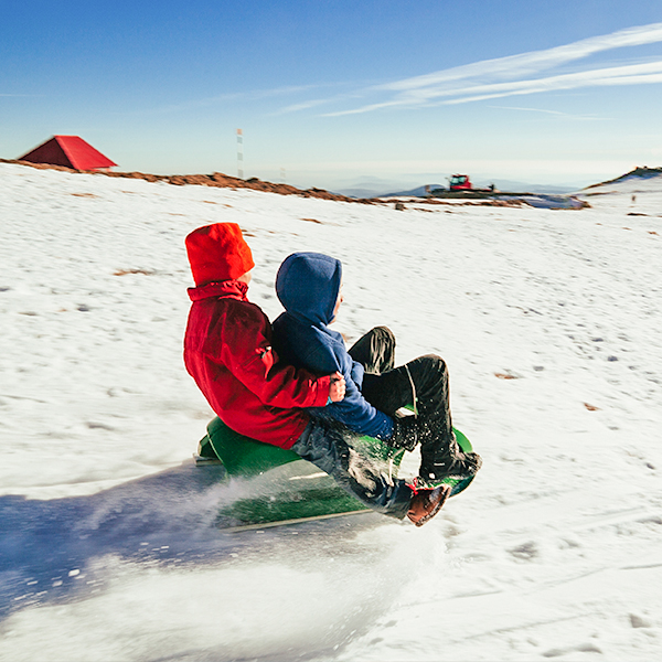 Two children, one in red and the other in a blue coat, sleigh together