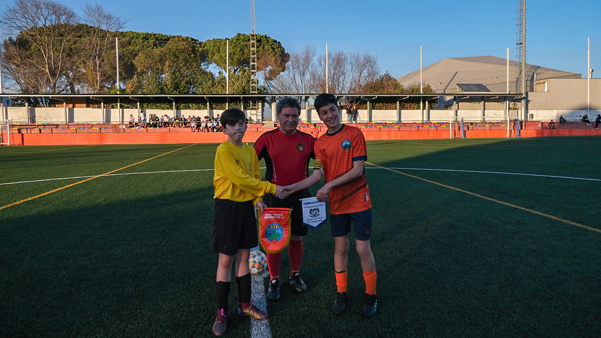 Captains of a UK school in yellow and local Spanish side in orange exchange club pennants on a pitch