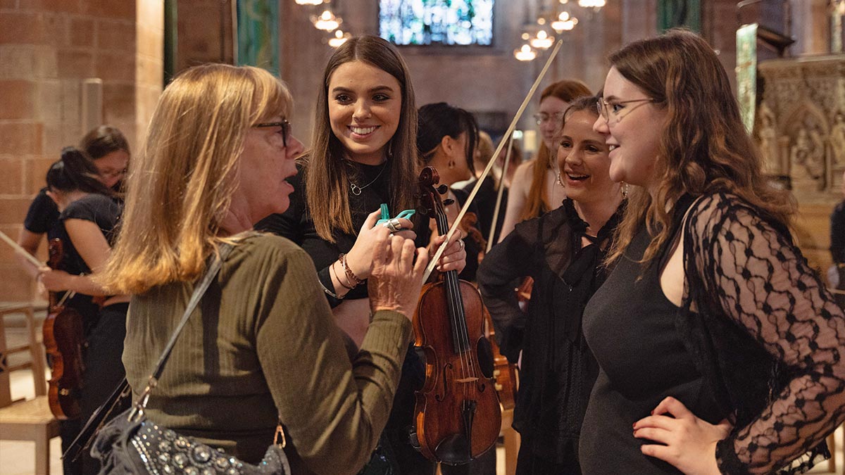 Three musicians, one with a violin, listen to an audience member