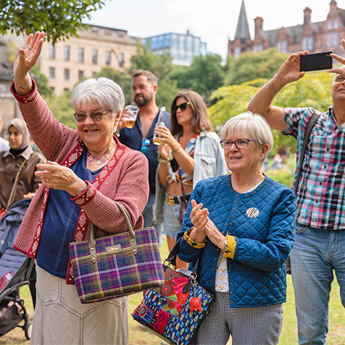 Audience members dance, clap and record as they enjoy an outside performance