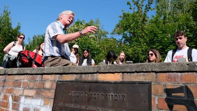 Field Sudy Tutor perched on wall at Platform 17 Memorial at Grunewald Station in Berlin talking to a group of students