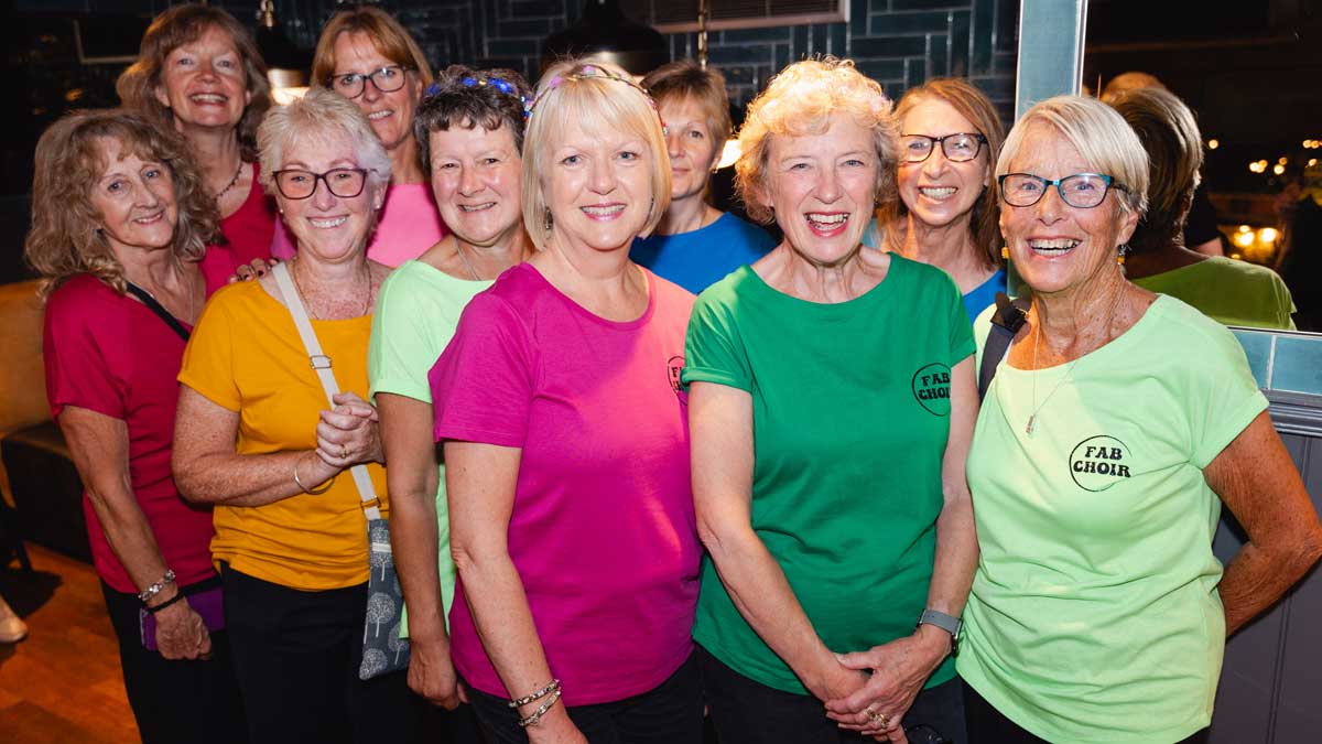 Choir members in vibrantly coloured t-shirts pose for the camera