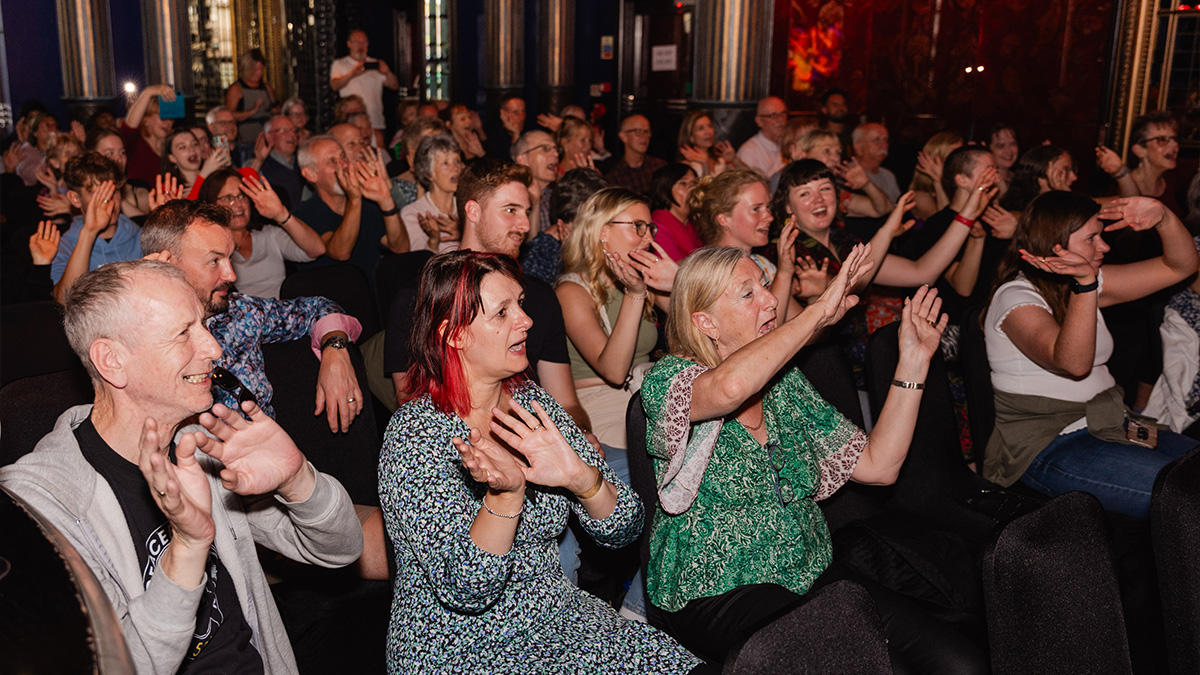 Audience sing and wave hands during Fab Choir's Le Monde performance at the Edinburgh Fringe Festival.