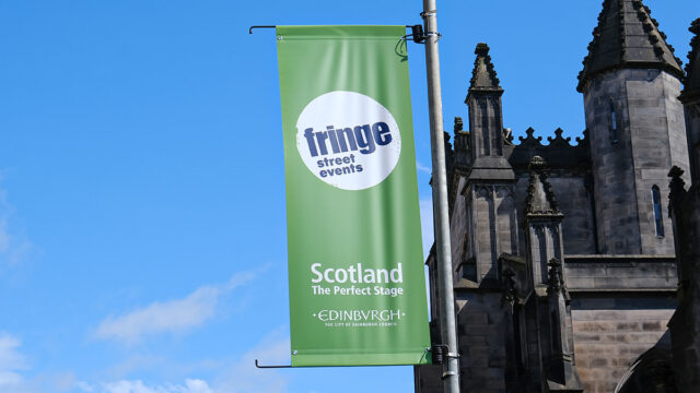 Edinburgh Fringe green flag attached to a streetlamp with St Giles in the right background.