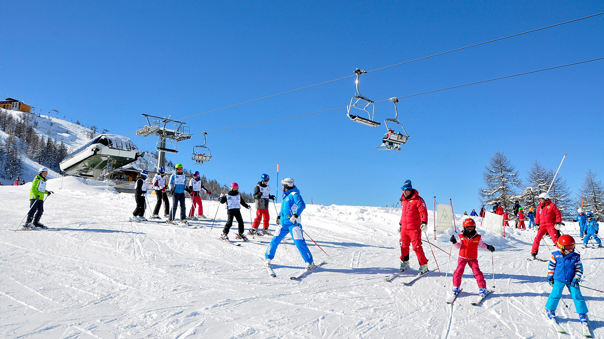 Skiers by the chair lift on a snowy mountain with blue skies in Sestriere ski resort.