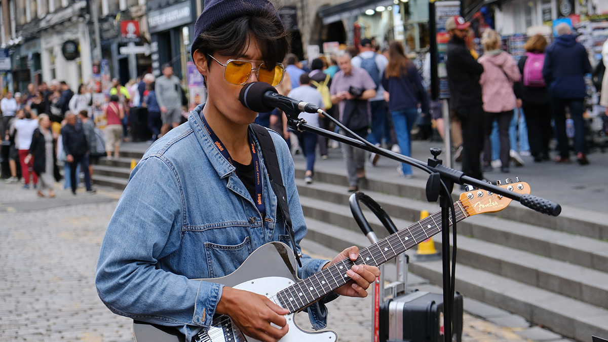 A trendy guitarist plays and sings on the Royal Mile during the Edinburgh Fringe.