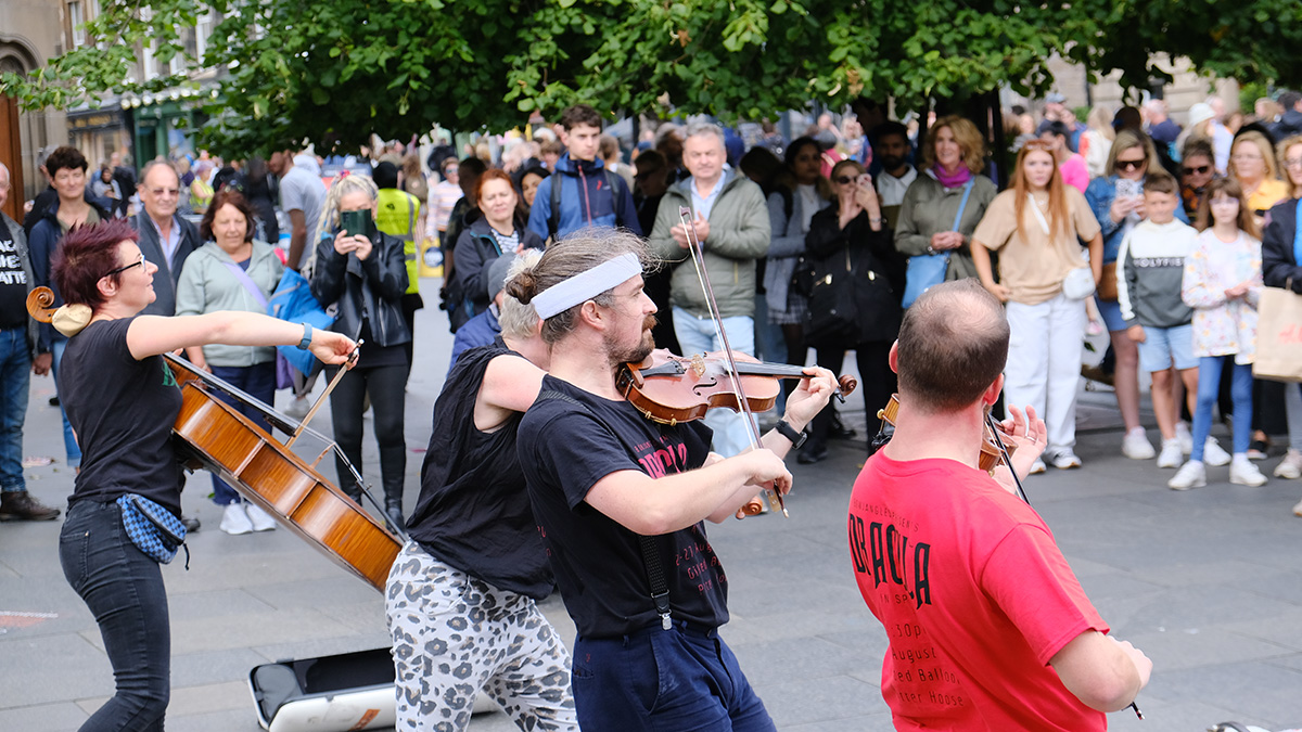 Band of violinists and a cellist perform on the street to a Edinburgh Fringe audience.