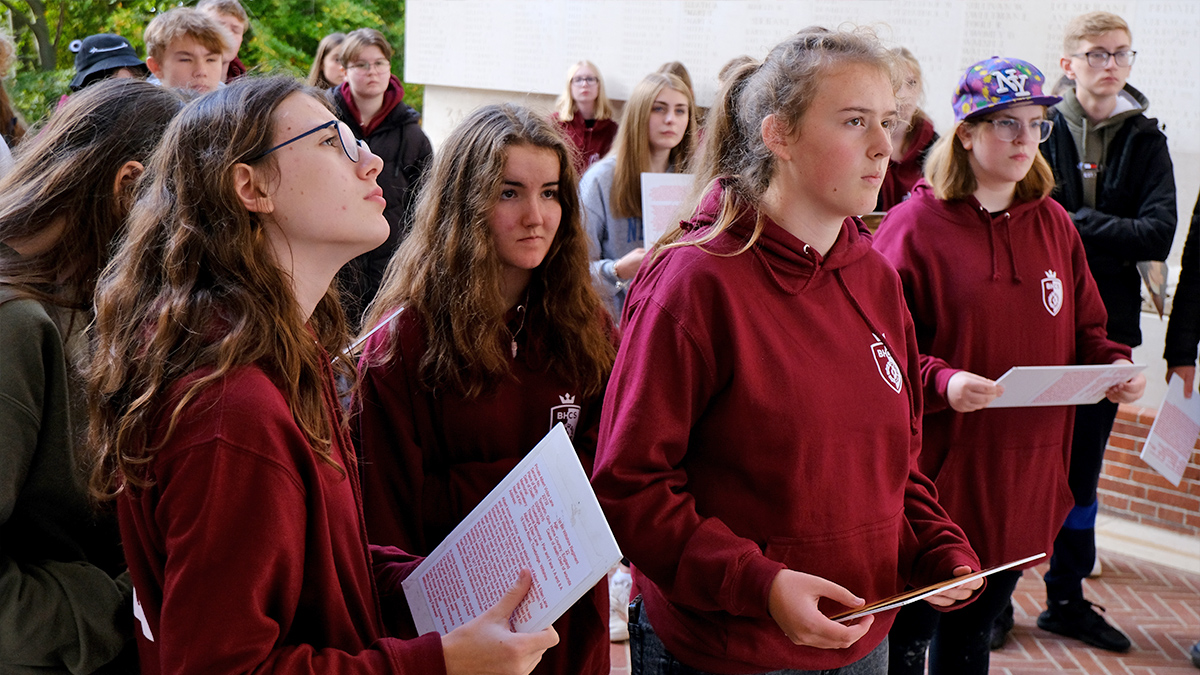 Students listen to a speaker off camera whilst at a memorial.