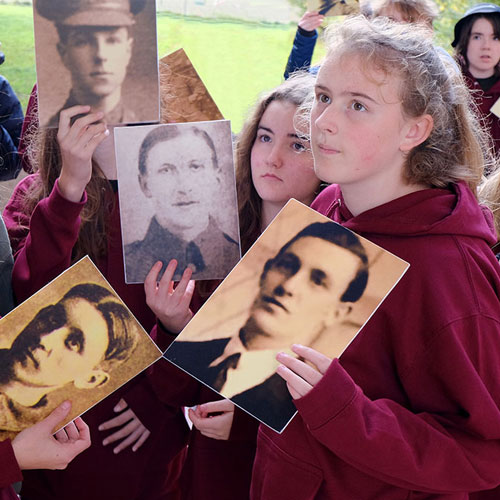 Students hold photos of soldiers from the World Wars whilst at a memorial.