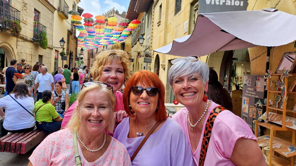 Four choir members from Caritas Harmony smile and pose for the camera with Poble Espanyol behind them