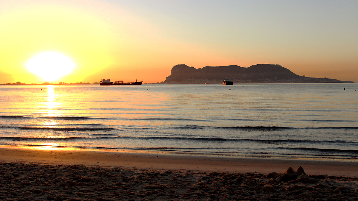 Sunset over the sea on a beach in Gibraltar with a mountain in the background