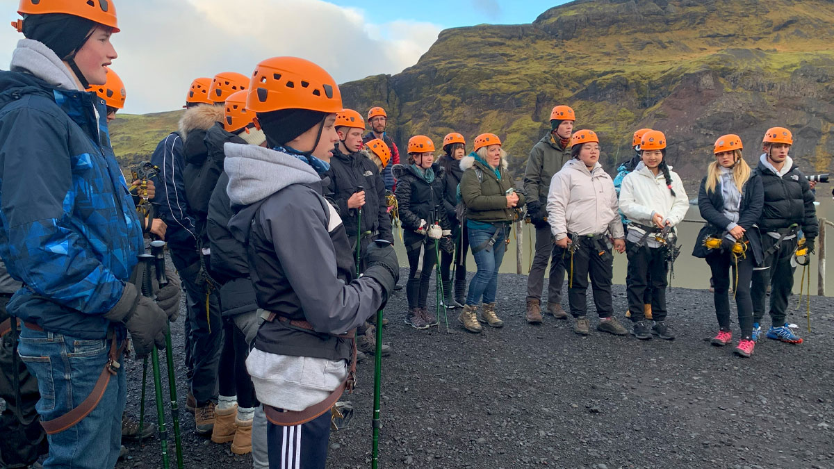 Students stood on black sand focusing with a mountain backdrop.