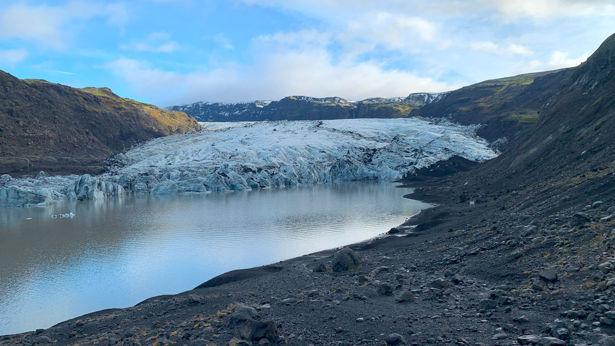 Sólheimajökull glacier as a landscape with black sands and a lake in front.