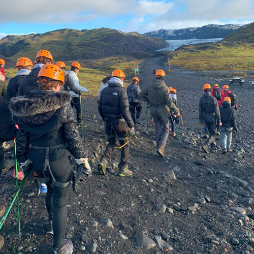 A group of students walking towards a glacier on black sand. Sólheimajökull Glacier is in the background.