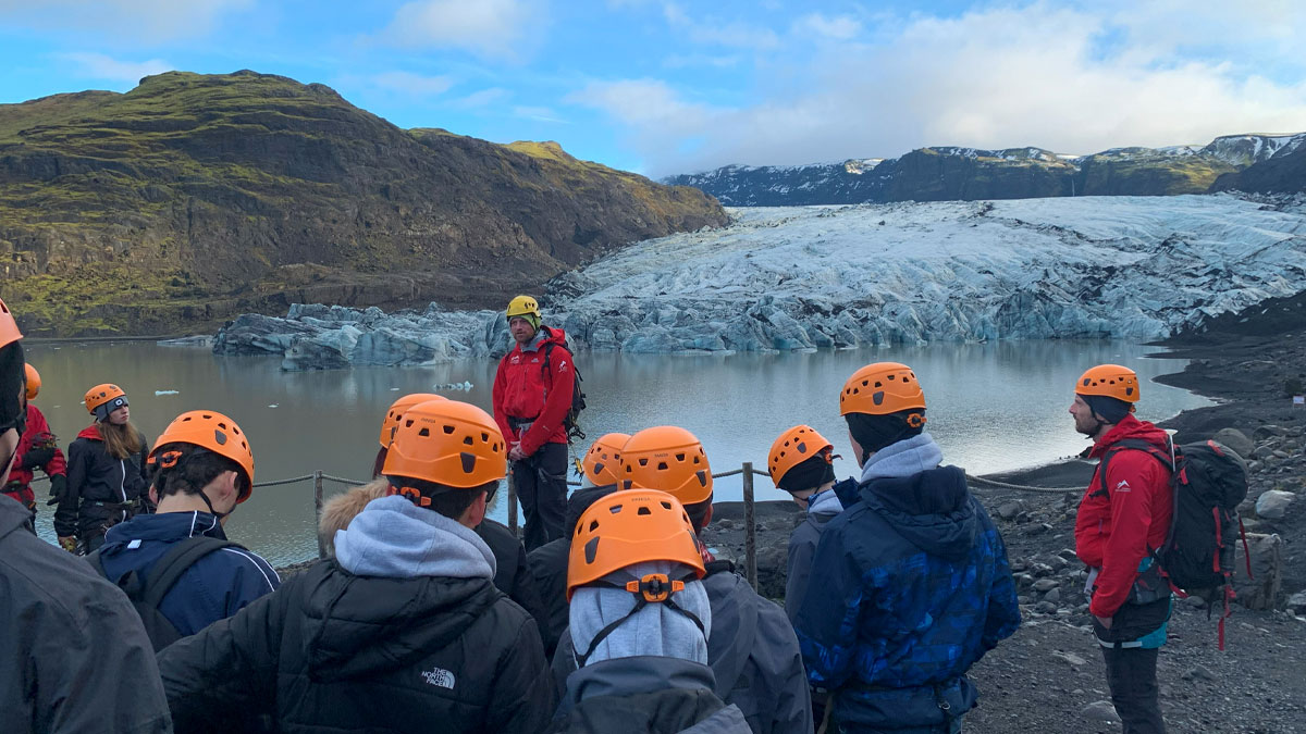 Sólheimajökull glacier in the backdrop with students facing towards it listening to a guide