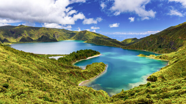 Lagoa do Fogo on the Azorean island of Sao Miguel, on a clear, bright day, surrounding by lush green vegetation.