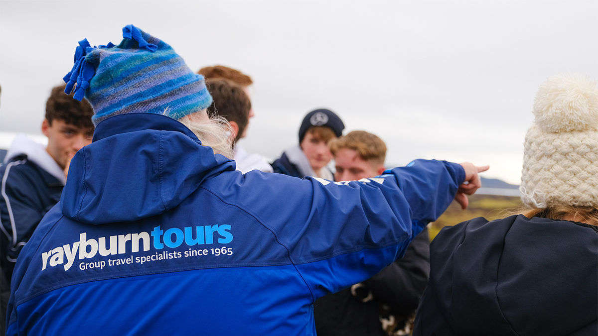 Field Study Tutor, with a Rayburn Tours coat, engages a group of students and points off camera.