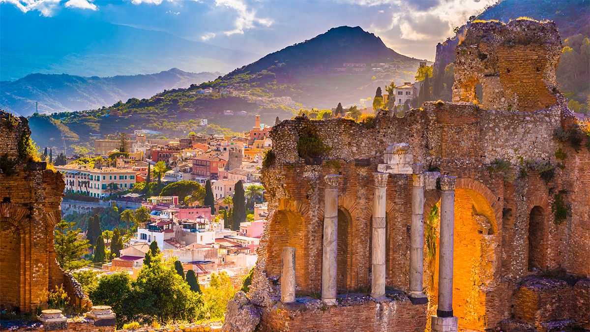 Taormina ruins in the foreground with Mount Etna, Taormina and Sicily in the background.