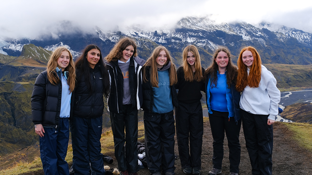 A group of girl students pose with the mountains of Iceland in the background.