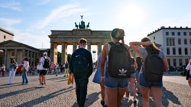Students walking towards brandenburg gate in the sun on a busy day