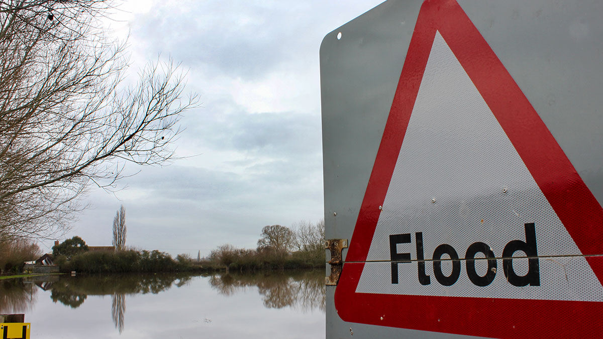 Flood Sign Warning by Flood. UK flood sign overlooking flooded land in rural area.