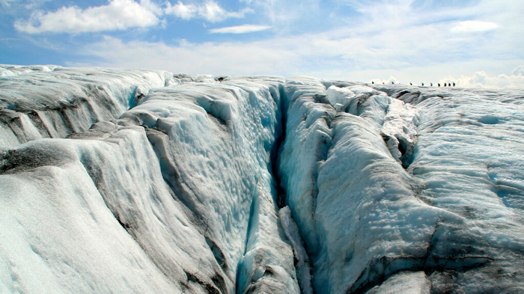 Hikers trekking across the blue crevassed ice of Folgefonna glacier in Norway. Hikers crossing dramatic ice formations of Folgefonna glacier in southern Norway on a guided trek through blue crevasses.