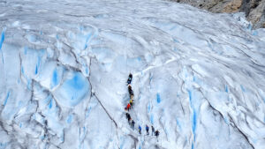 Hikers trekking across the blue crevassed ice of Folgefonna glacier in Norway. Hikers crossing dramatic ice formations of Folgefonna glacier in southern Norway on a guided trek through blue crevasses.
