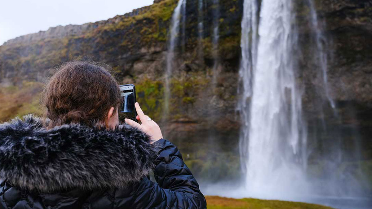 Student taking a photo of a waterfall in Iceland