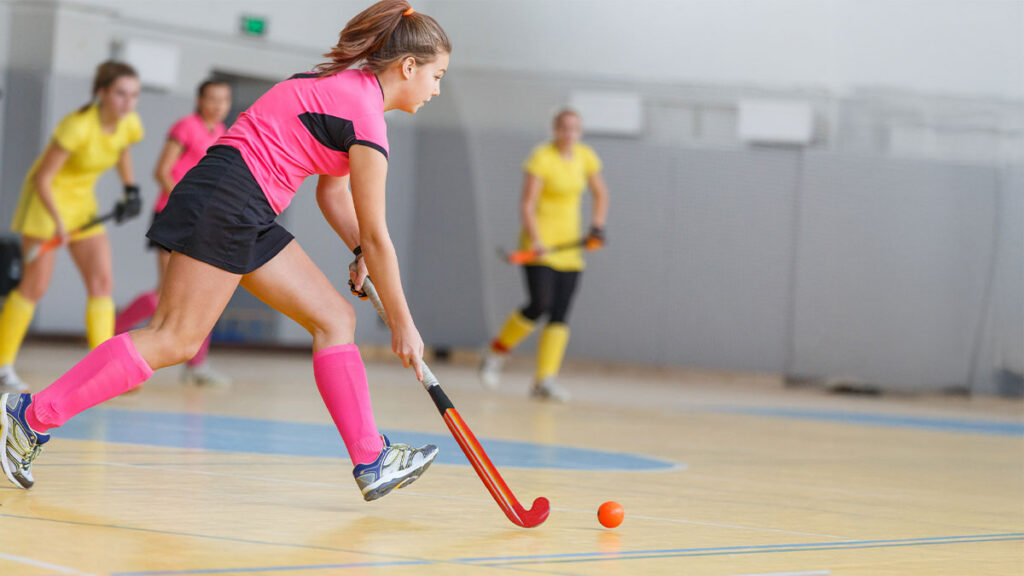 Young woman hockey player in attack at indoor hockey match