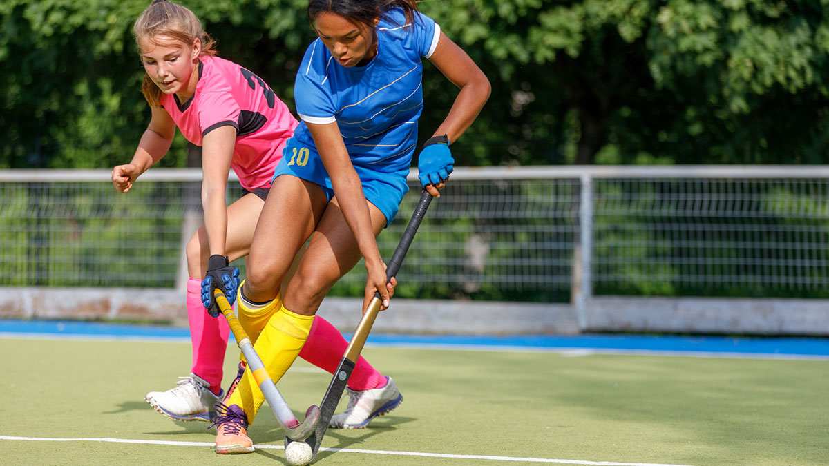 Two young female athletes compete in intense field hockey match during sunny day. Two female players engage in a competitive field hockey match on a bright, sunny day.