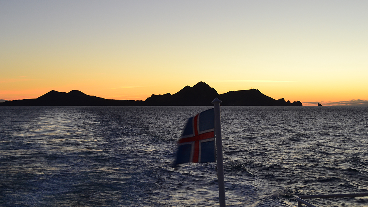 picture of the sea looking back to Heimaey with an Iceland flag in the centre of shot